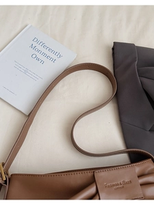 Detail of a brown pleated leather bucket bag with embossed logo and shoulder strap