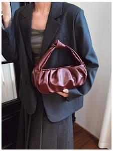 Detail of burgundy ruched leather shoulder bag with knotted handle on grey blazer