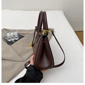 Detailed side view of dark brown leather tote bag with gold buckle and trapezoid structure
