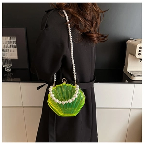 Detail of neon acrylic shell evening bag with faux pearl handle on a black wool coat