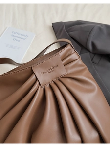 Macro detail of brown leather tote showing accordion pleats and embossed fashion logo