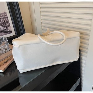 Close-up of minimalist off-white leather tote bag with unique circular handle on black table