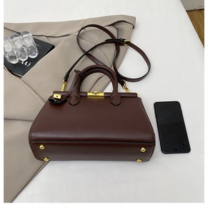Deep brown briefcase handbag with gold hardware and shoulder strap in a business setting