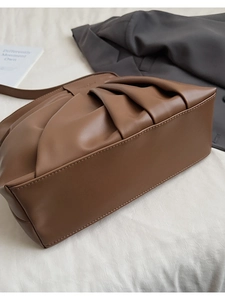 Detail of a brown pleated faux leather bucket bag on white fabric with accessories