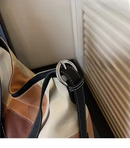 Detail of color-block shoulder bag with stitched black strap and silver buckle hardware