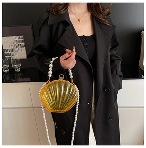 Detail view of shell-shaped orange acrylic handbag with pearl strap on black coat