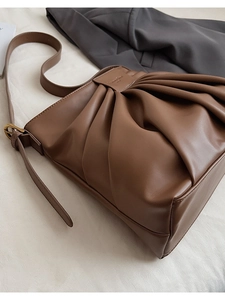 Detail view of caramel brown pleated leather bucket bag with brand logo and soft texture