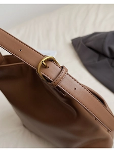 Detail of adjustable strap with vintage bronze buckle on brown matte leather bucket bag