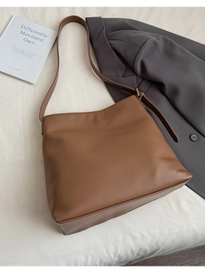 Brown leather tote bag with adjustable strap styled on white fabric with a blazer