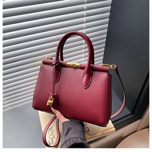 Close-up of burgundy leather handbag with gold lock and handle by a shuttered window