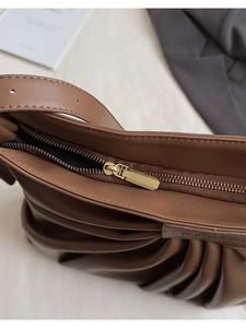 Detail of golden metal zipper closure on brown pleated leather bucket tote bag