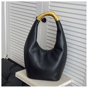 Dettaglio borsa a secchiello in pelle nera con manico in metallo dorato asimmetrico artistico