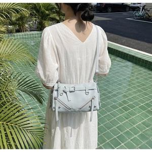 Detail of light blue motorcycle style shoulder bag with zippers and metal rivets