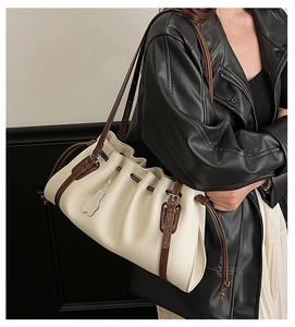 Detail of cream pleated tote bag featuring contrast brown leather straps and metal buckle