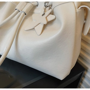Detailed shot of cream drawstring tote bag featuring leather star pendant and soft texture