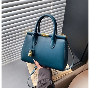 Detail view of teal leather handbag featuring a gold padlock and adjustable shoulder strap