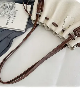 Detail view of cream pebble leather bucket bag with brown straps and drawstring closure