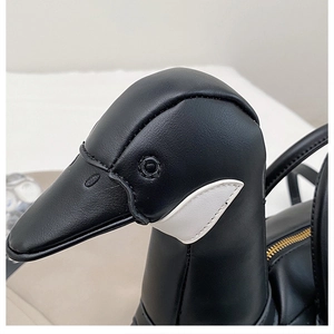 Détail d'un sac à main en cuir noir en forme d'oie avec fermeture éclair dorée et patchs blancs