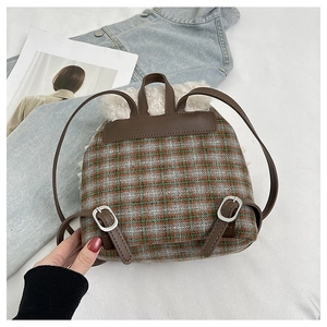 Dettaglio mini zaino a quadri con ecopelliccia e cinturini in pelle marrone su letto bianco