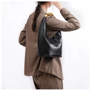 Dettaglio borsa a secchiello in pelle nera minimalista con manico in metallo dorato