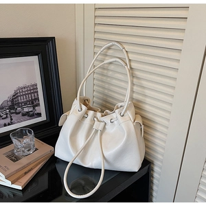 Detail of white drawstring bucket bag with side pockets and smooth matte leather texture