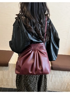 Detail of burgundy pleated bucket bag with embossed leather tag and soft PU texture