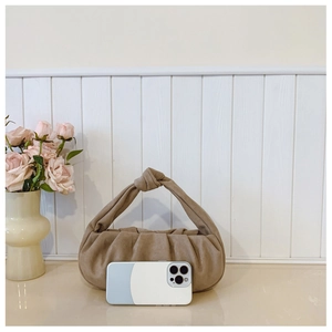 Detail of beige pleated dumpling bag featuring unique knot handle and mobile phone for scale