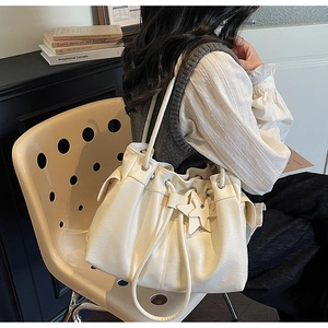 Detail of a creamy white leather tote bag with drawstring folds and star charm pendant