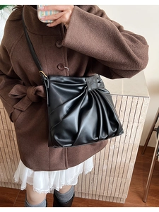 Detail of black pleated bucket bag showing the matte texture and metal buckle on shoulder strap