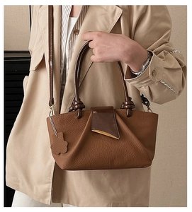 Detailed close-up of pleated leather handbag featuring metallic buckle and bear charm