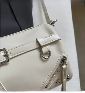Close-up of silver metal hardware and rivets on a beige leather cylinder crossbody bag