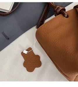 Detail of brown litchi grain leather bag featuring a floral petal shaped pendant