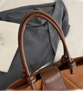 Close-up of brown textured leather handbag featuring knotted handle detail and premium grain
