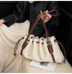 Close-up of cream pleated hobo bag with dark brown strap and cute bear leather charm