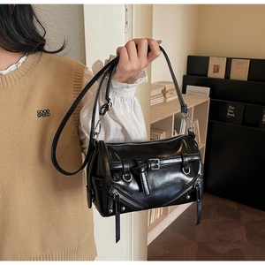 Close-up of a glossy black cylinder bag with silver zippers and buckle strap details