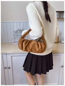 Detail of a pleated brown suede cloud bag showing soft texture and handle on a model