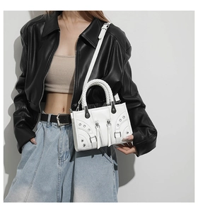 Detail of white motorcycle handbag featuring silver studs, zippers, and woven handle