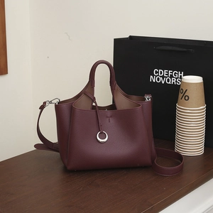 Detail of burgundy lychee leather tote bag featuring a silver ring charm and long strap