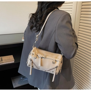 Detail of beige glossy shoulder bag with zippers and belt buckle on a model