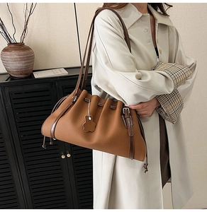 Detail of brown pleated leather tote with drawstring tassels and teddy bear pendant