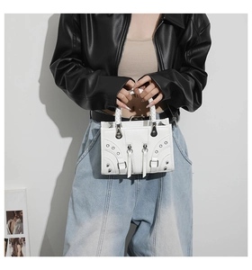 Close-up of white leather handbag featuring silver studs, zippers, and woven handles