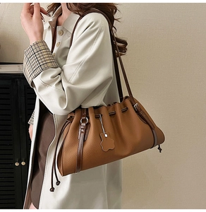 Detail of a brown pleated shoulder bag with a bear charm and adjustable drawstring strap