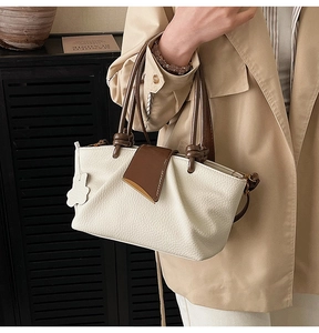 Detail of cream-colored pleated handbag with dark brown handle and a cute bear charm