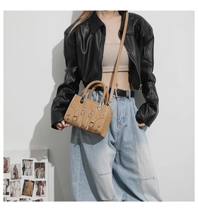 Detail of beige motorcycle bag with metal studs and woven handles worn with leather jacket