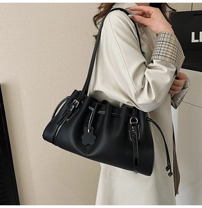 Detail of black pebbled leather tote bag featuring drawstring closure and cute bear charm