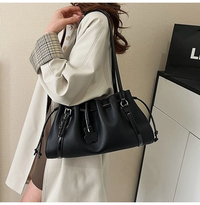 Detail of black lychee grain leather shoulder bag with drawstring and flower charm