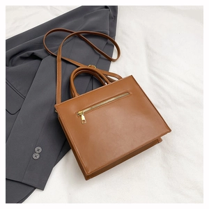 Detailed view of brown PU leather handbag featuring a horizontal gold metal zipper pocket