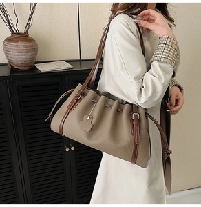 Detail of a large textured leather shoulder bag featuring a drawstring closure and logo tag