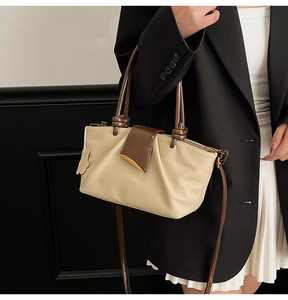 Detail of beige pleated handbag with brown handles and gold hardware on black suit