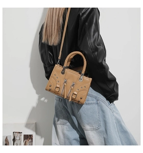 Detail of camel leather handbag featuring braided handles and punk-style metal studs
